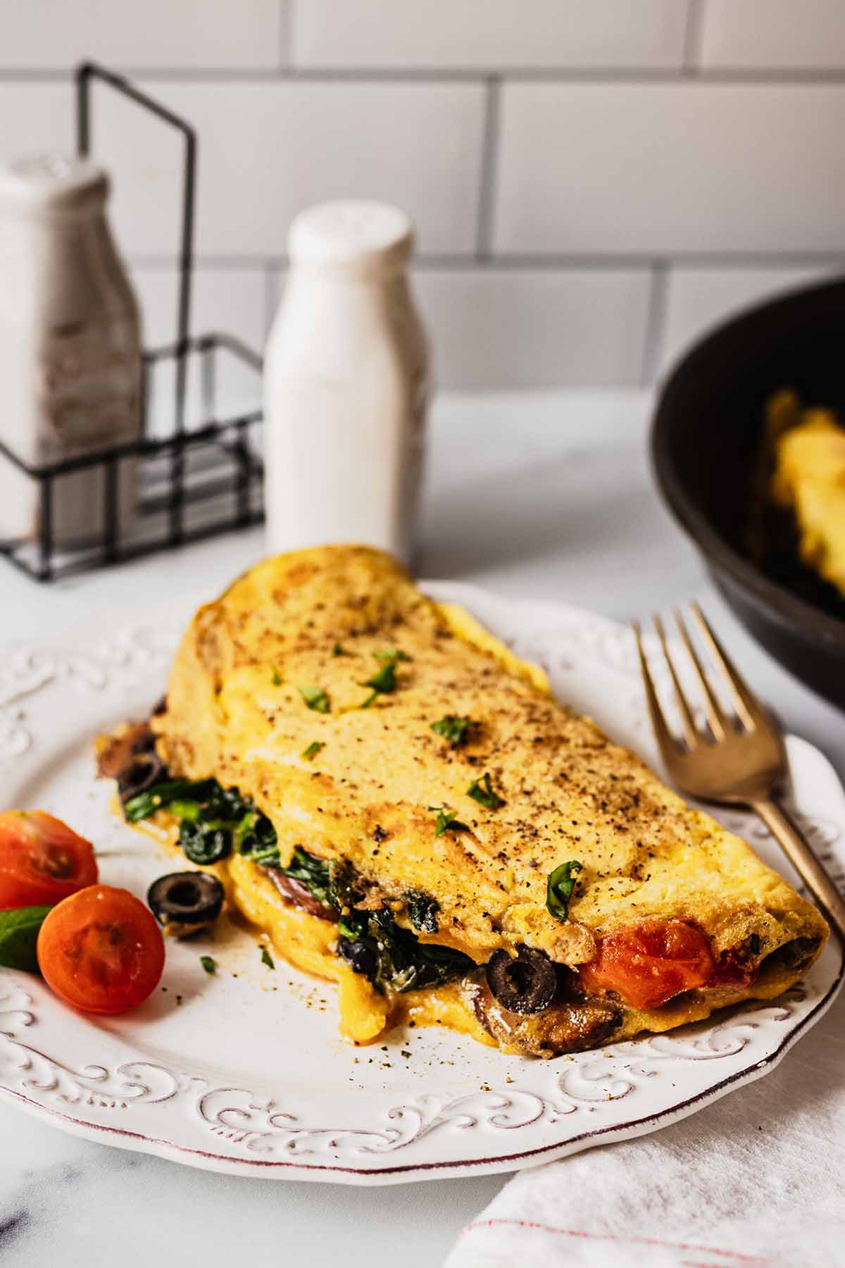 Vegetable omelette on a white plate with tomatoes, basil and a gold fork