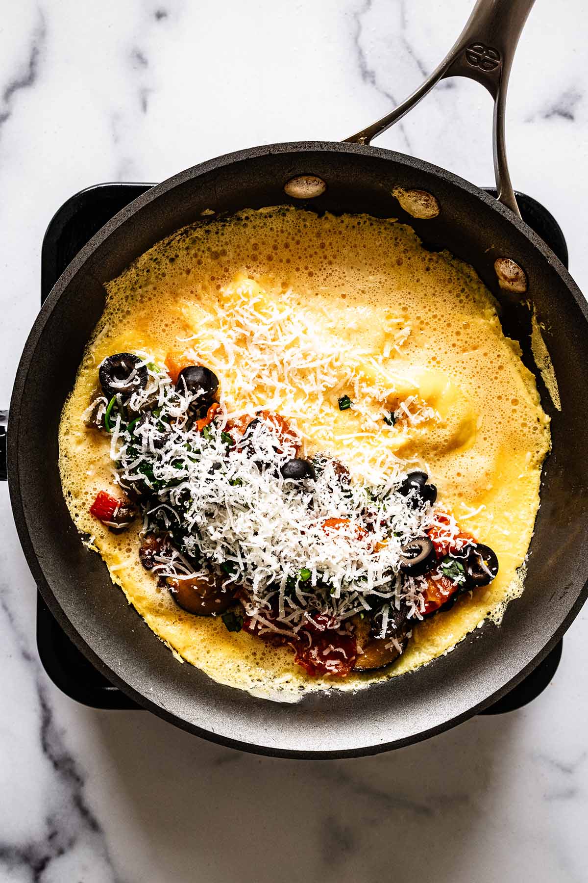 Grated Parmesan cheese on cooked vegetables on top of omelette in a skillet