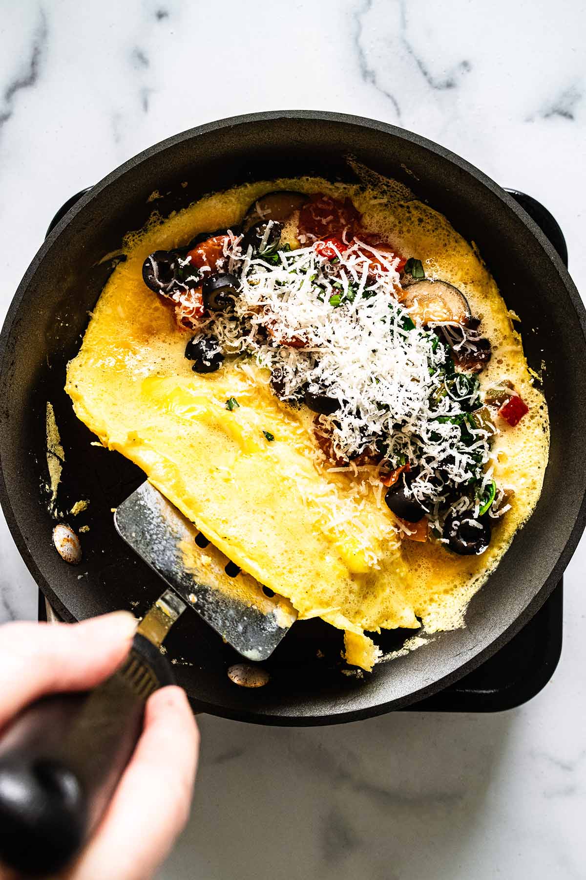 Spatula lifting unfilled half of omelette in a skillet