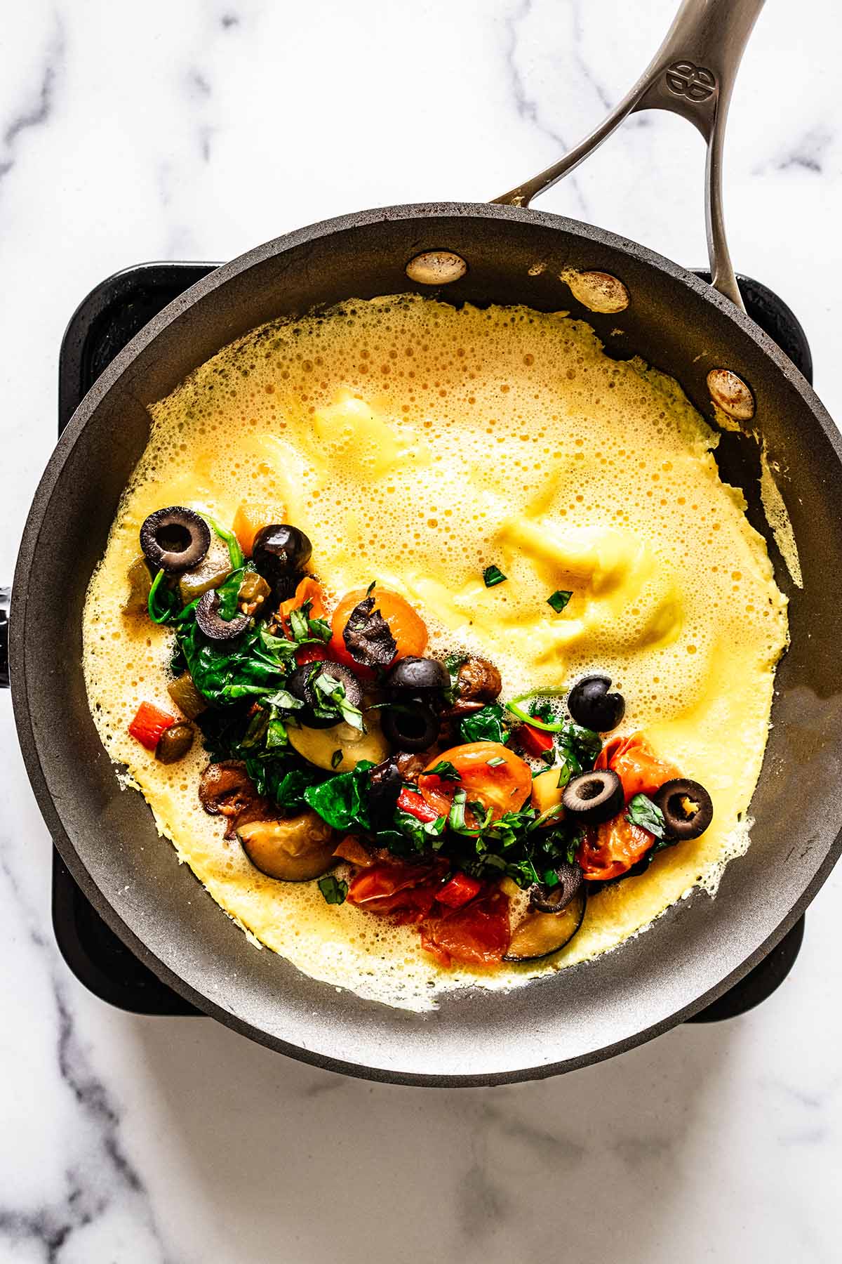 Vegetable mixture on one half of an open omelette in a skillet
