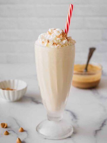 Butterscotch milkshake in a tall glass with whipped cream and a red and white straw