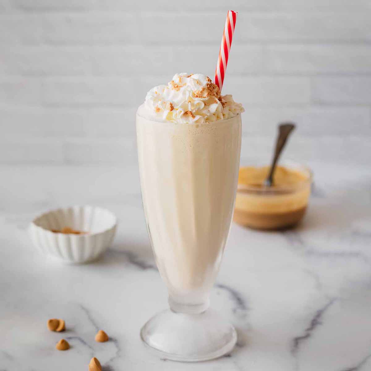 Butterscotch milkshake in a tall glass with whipped cream and a red and white straw