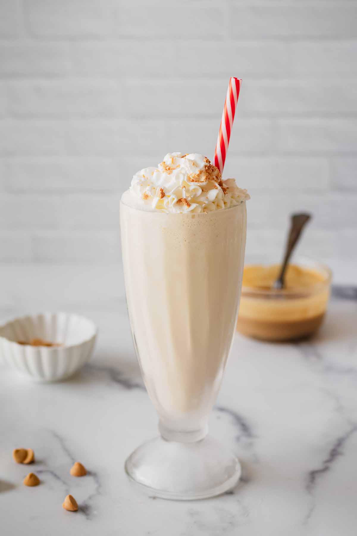Butterscotch milkshake in a tall glass with whipped cream and a red and white straw