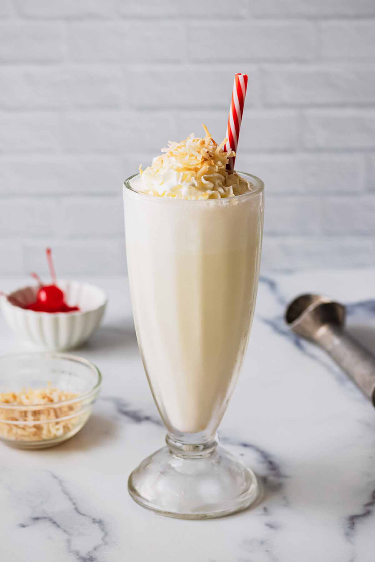 Coconut shake topped with whipped cream, and toasted coconut in a tall glass with a red and white straw