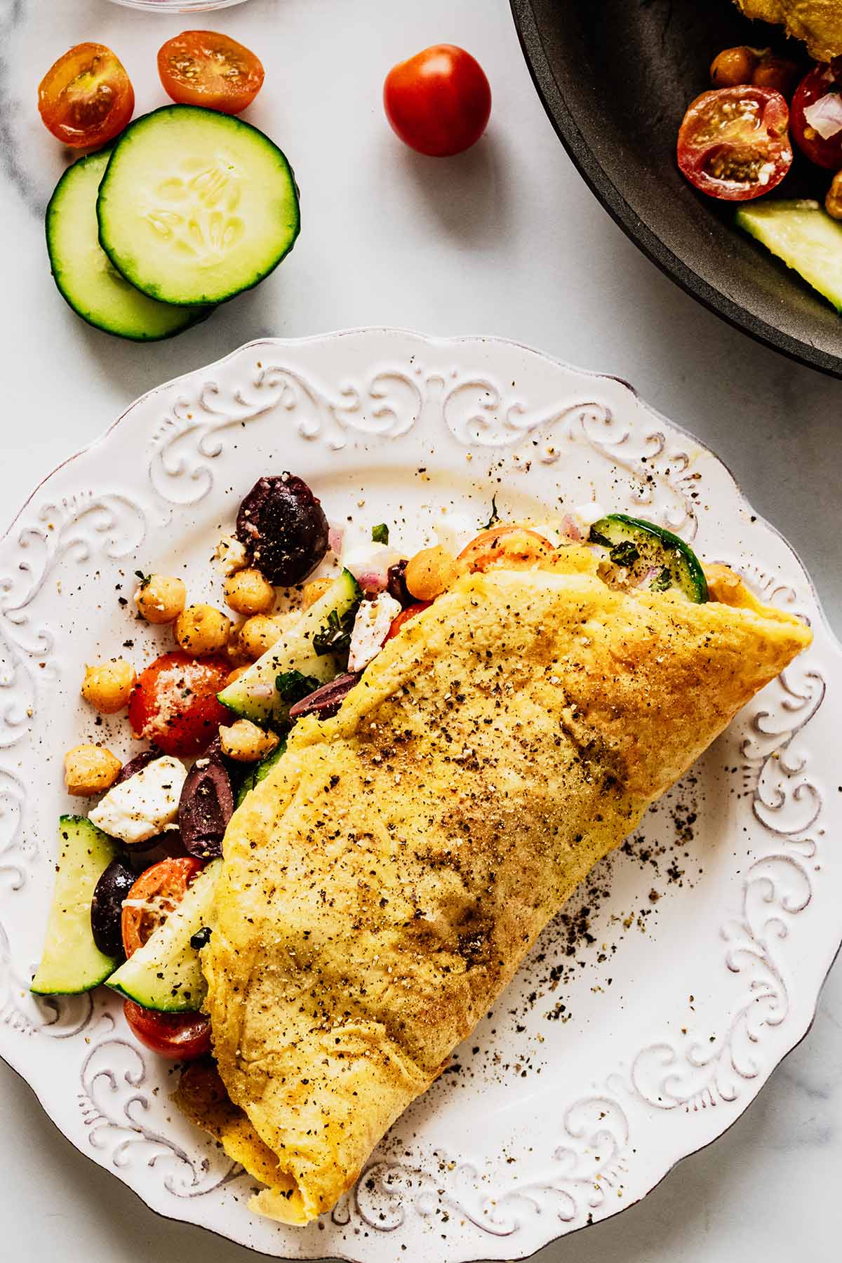 Overhead view of a Greek omelette on a white plate with filling spilling out and topped with fresh pepper