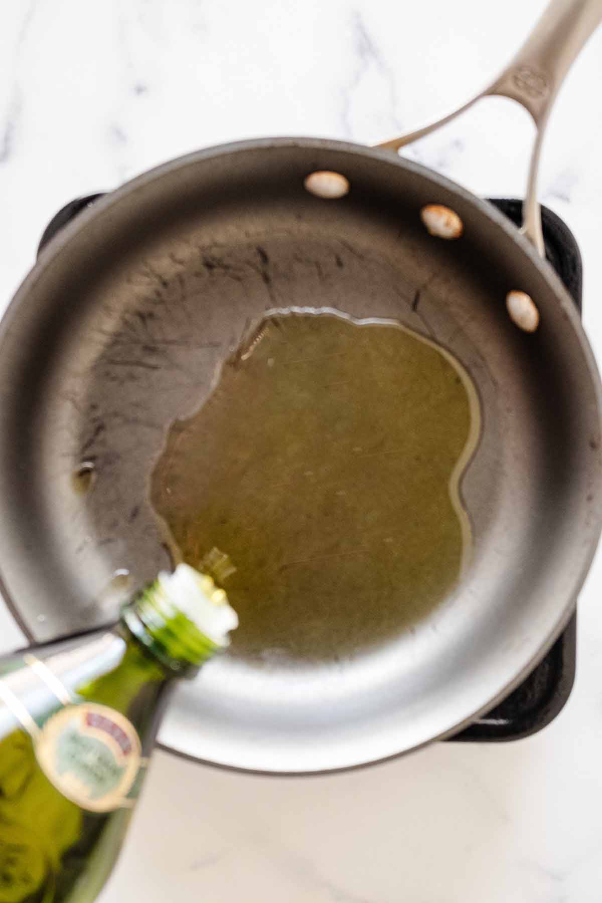 Overhead view of olive oil being poured into a skillet