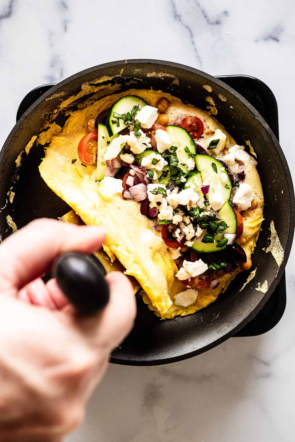 Overhead view of spatula folding unfilled side of omelette over filled side in a skillet