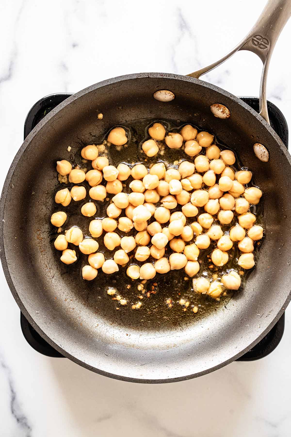 Overhead view of chickpeas and garlic cooking in a skillet