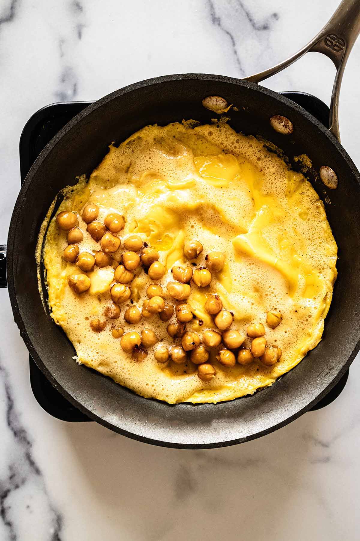 Overhead view of browned chickpeas on top of half of omelette in a skillet