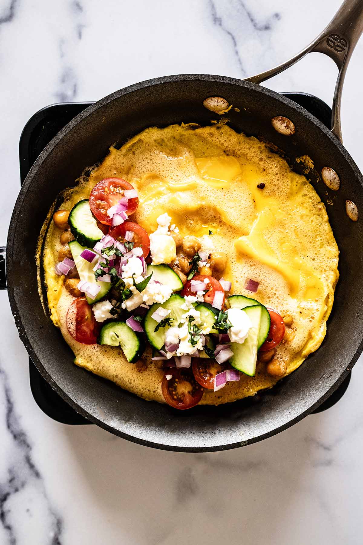 Overhead view of Greek omelette fillings on top of half of omelette in a skillet
