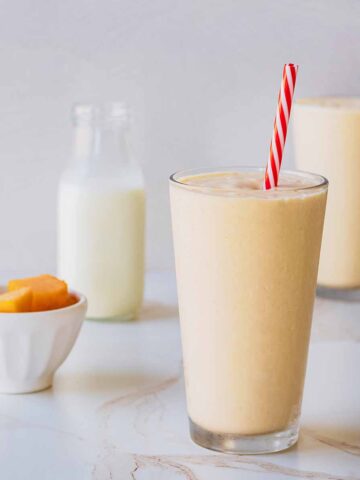Front view of two smoothies in tall chilled glasses with red and white straws