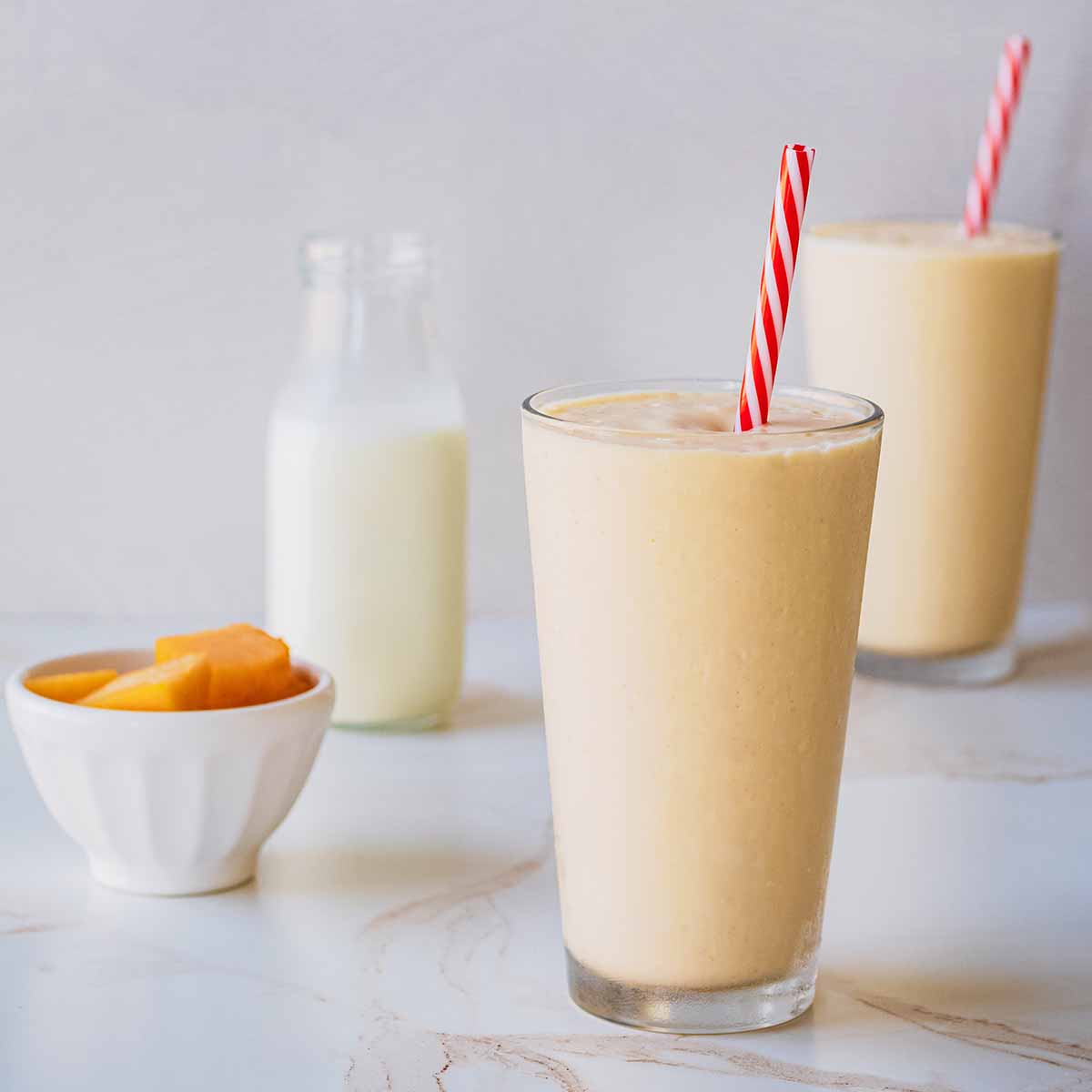 Front view of two smoothies in tall chilled glasses with red and white straws