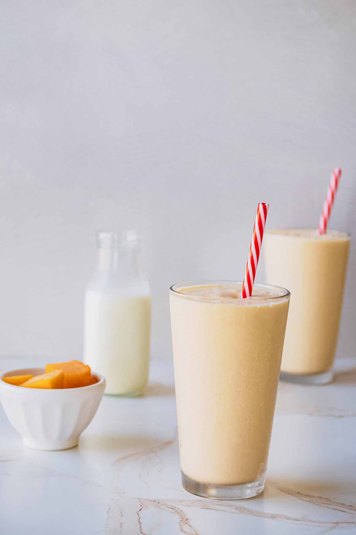 Front view of two smoothies in tall chilled glasses with red and white straws