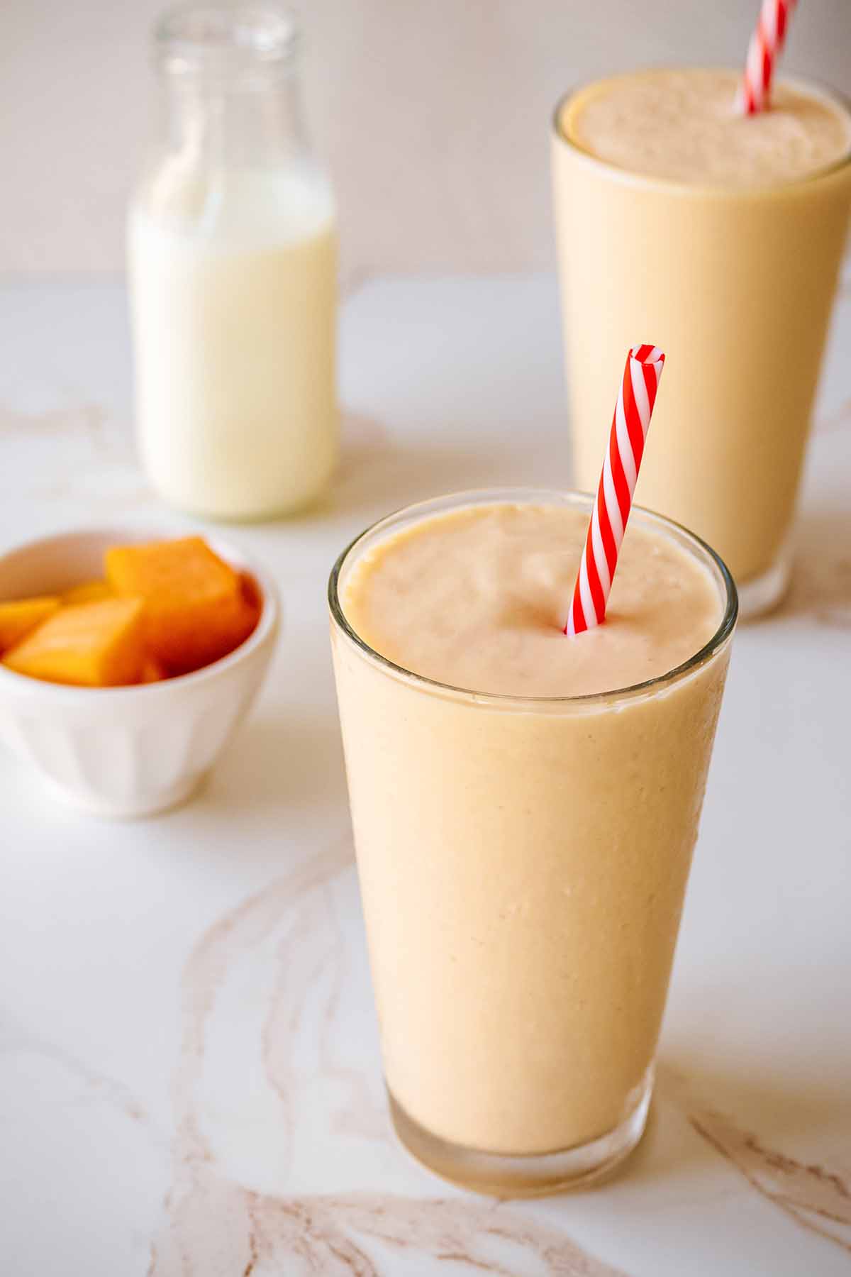 Two papaya smoothies in tall glasses with red and white straws