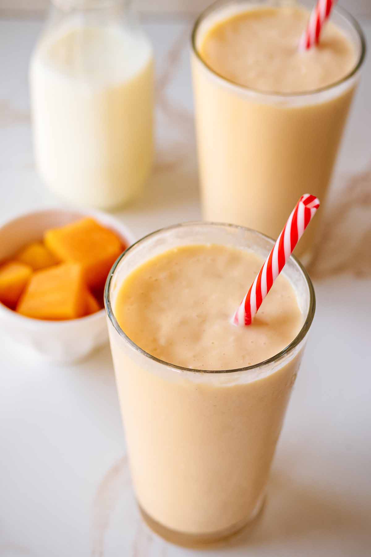 Overhead view of two smoothies in glasses with red and white straws