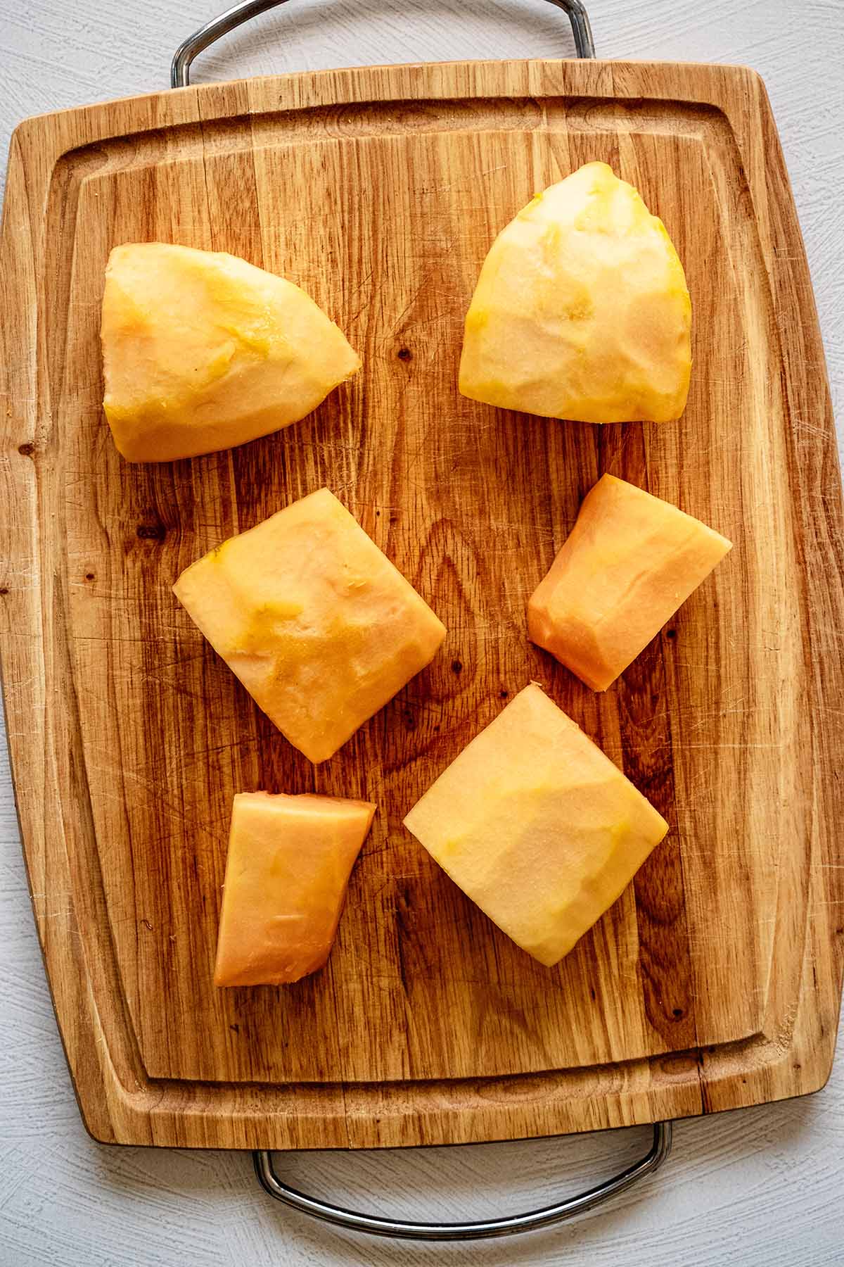 Large pieces of peeled papaya on a cutting board.