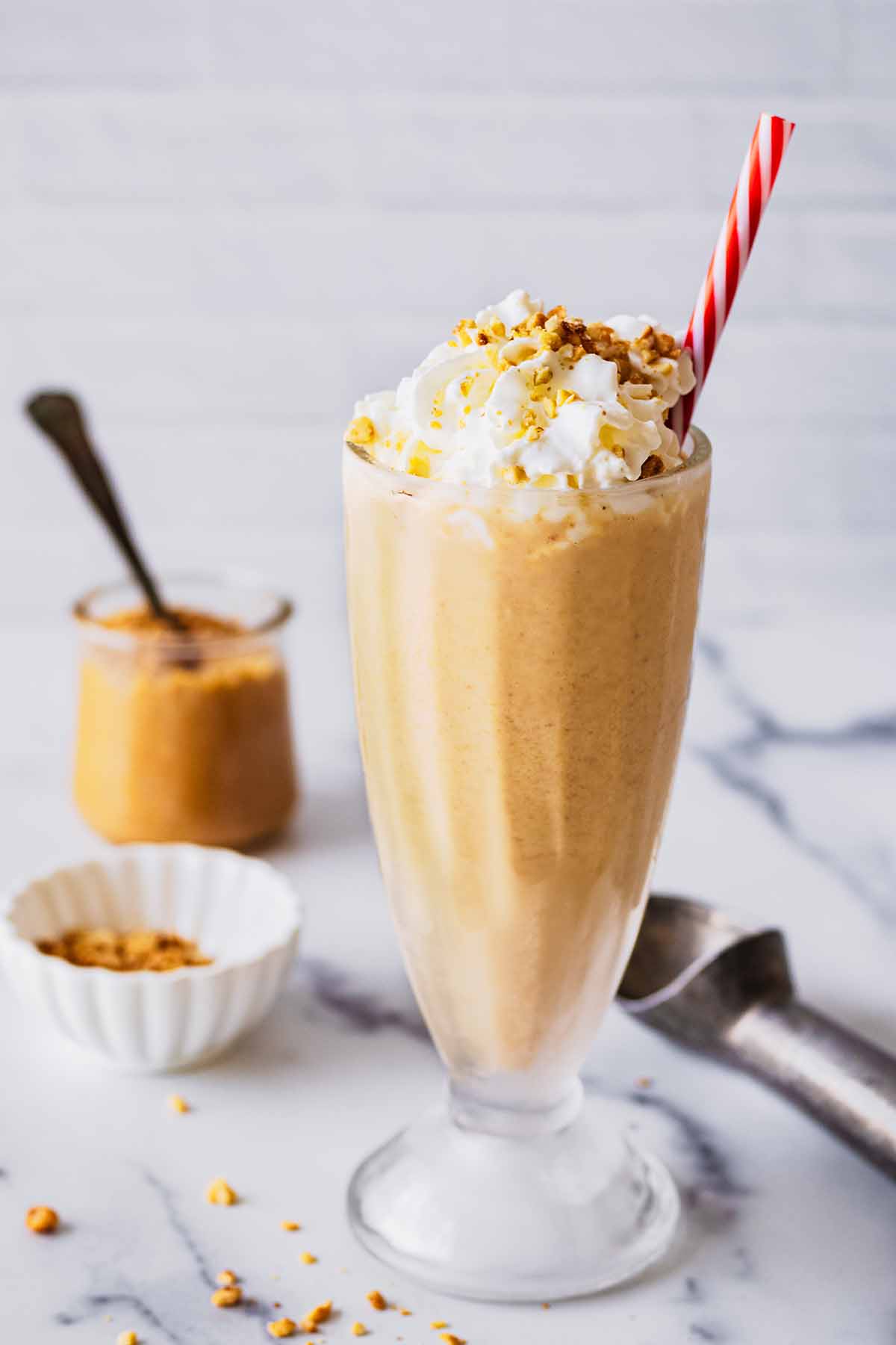 Peanut butter milkshake in a tall glass with whipped cream and a red and white straw.