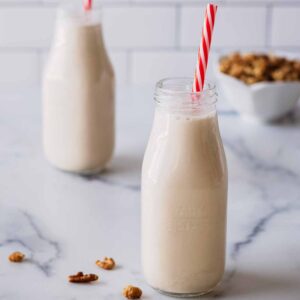 Walnut milk in two small milk bottles with red and white straws