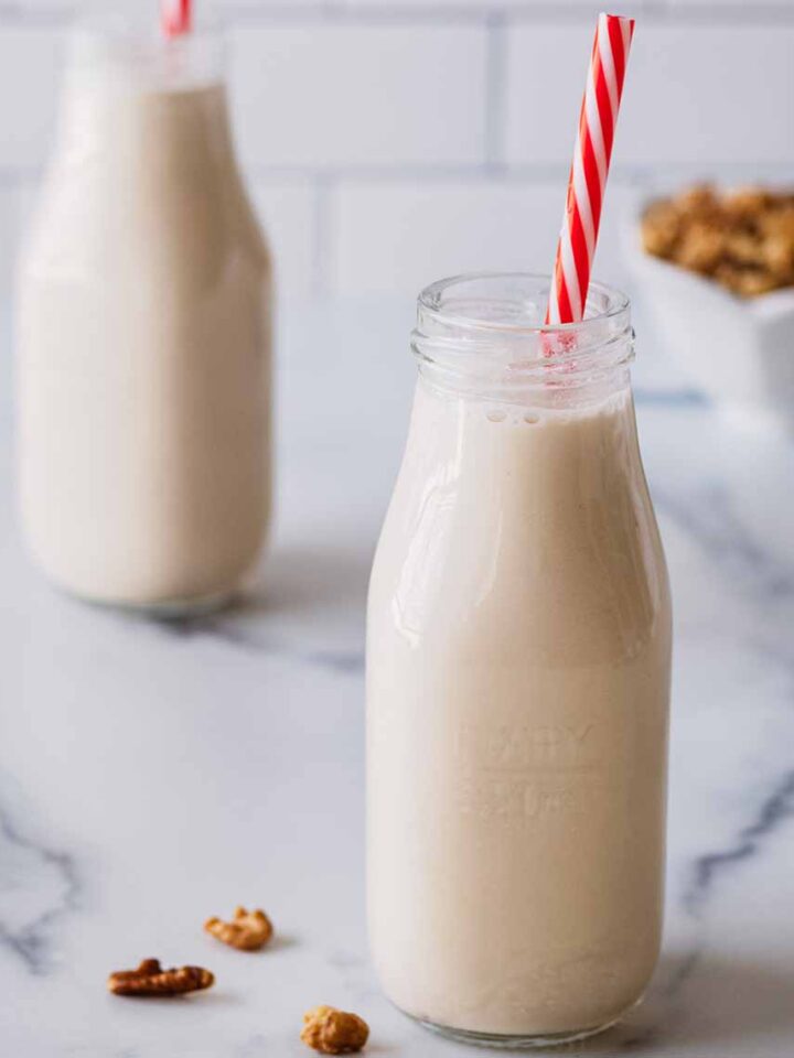 Walnut milk in two small milk bottles with red and white straws