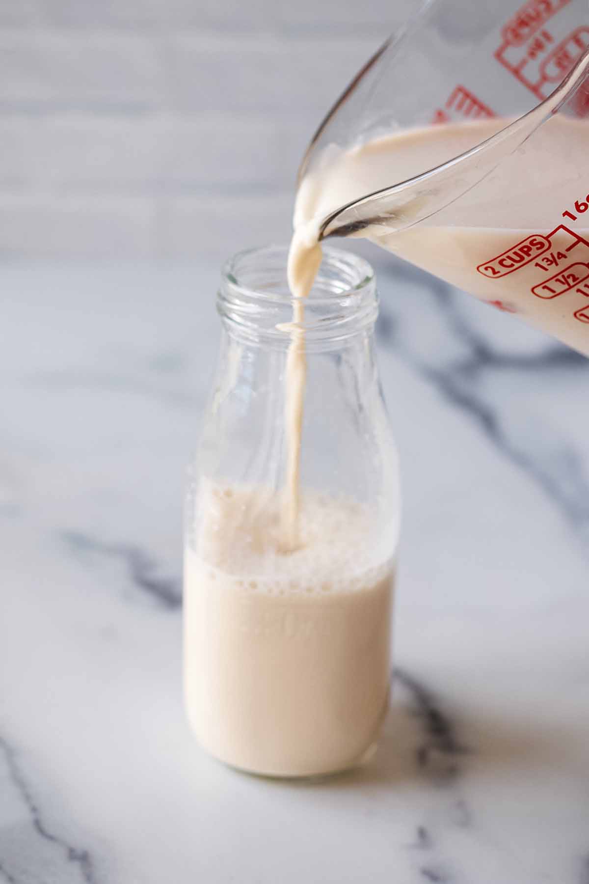 Walnut milk being poured into a small milk bottle