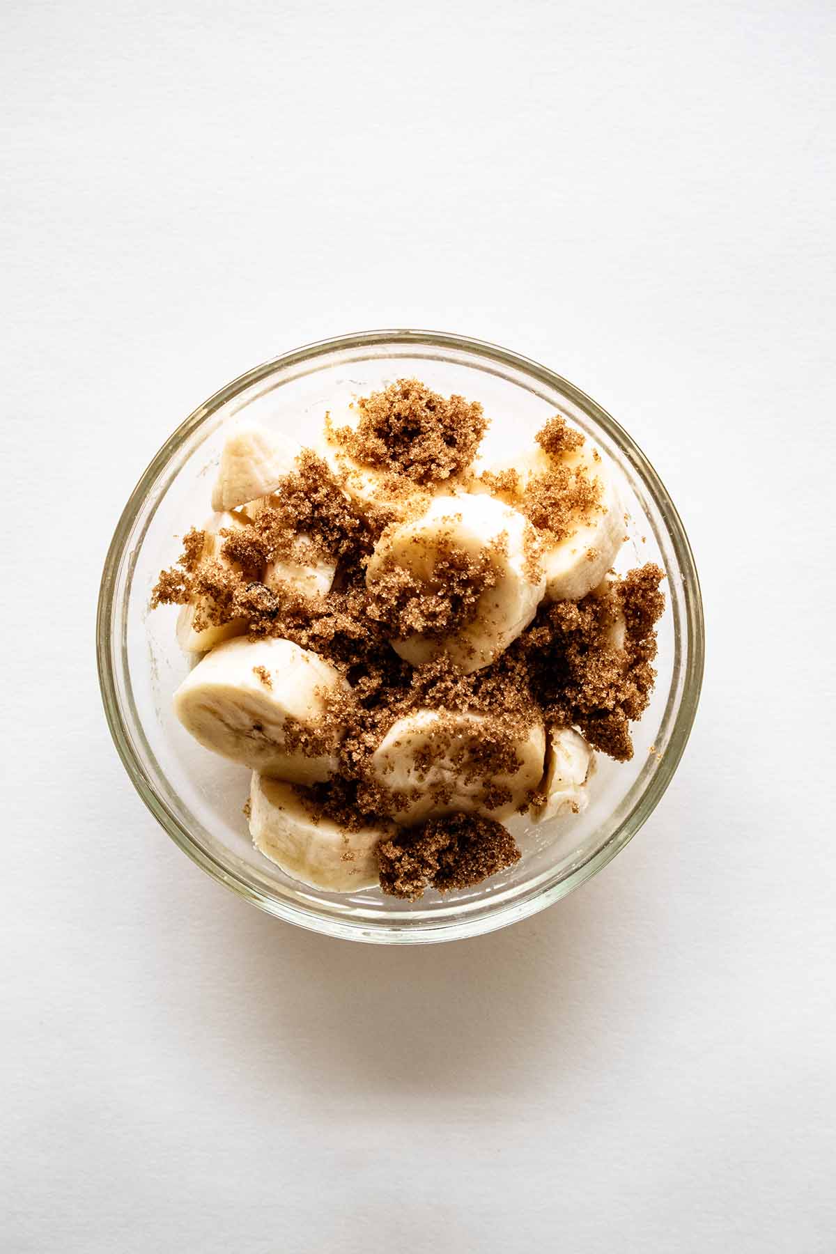 Overhead view of sliced bananas and brown sugar in a glass bowl