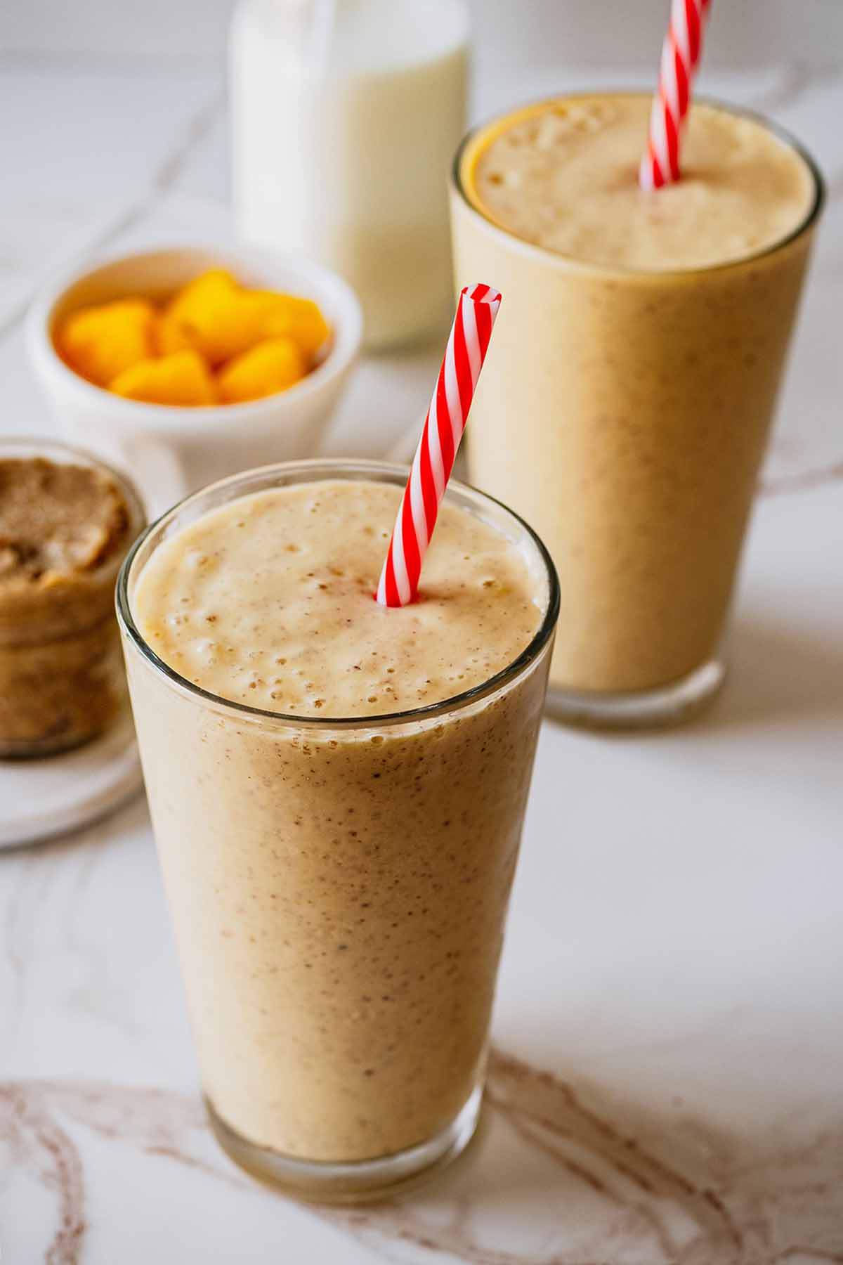 Two smoothies in tall glasses with red and white straws