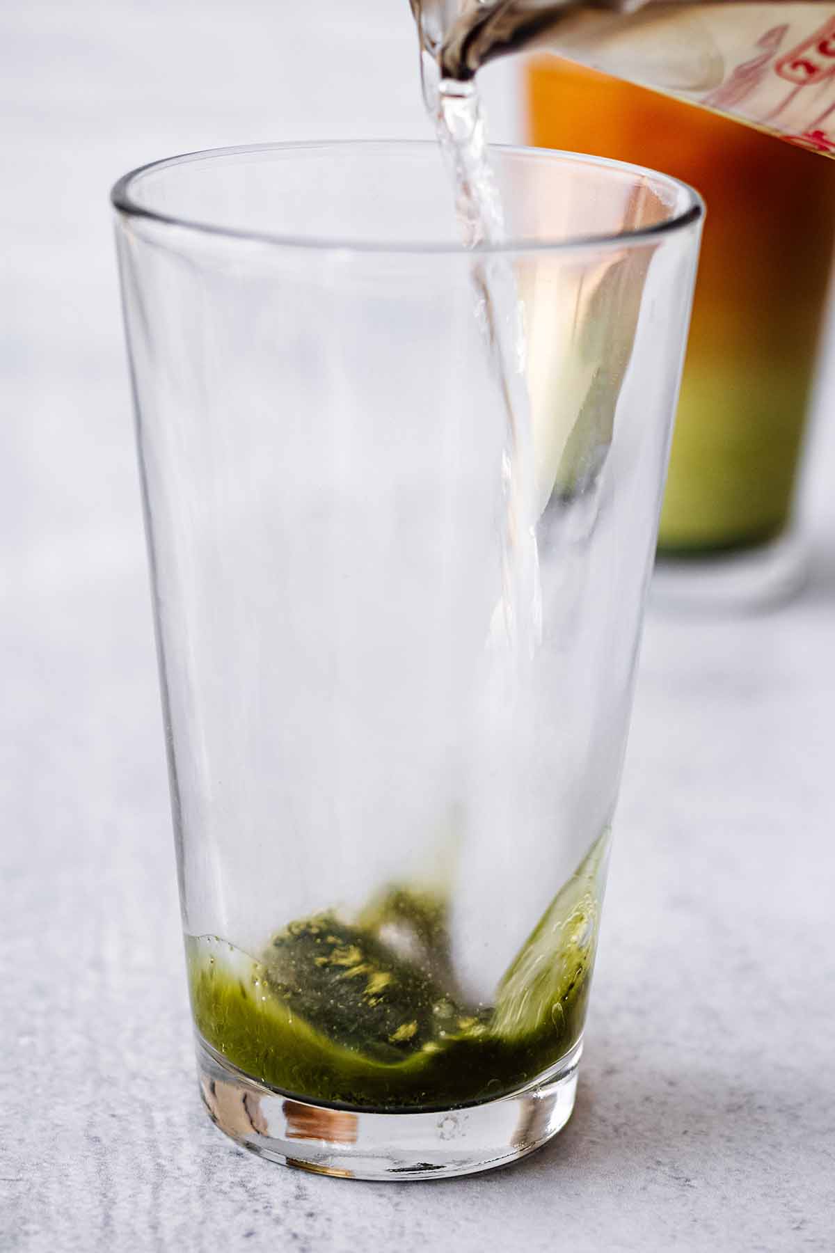 Hot water being poured in a tall glass with matcha powder and sweetener