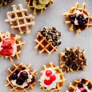 Overhead view of mini waffles with various toppings on a concrete background