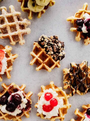 Overhead view of mini waffles with various toppings on a concrete background