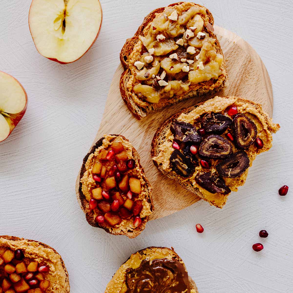 Overhead view of peanut butter toast with various toppings - sliced dates, sliced bananas, chopped apples, and Nutella