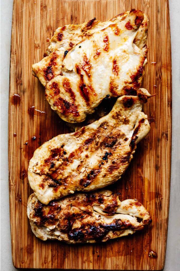 Overhead view of three grilled chicken breasts on a cutting board