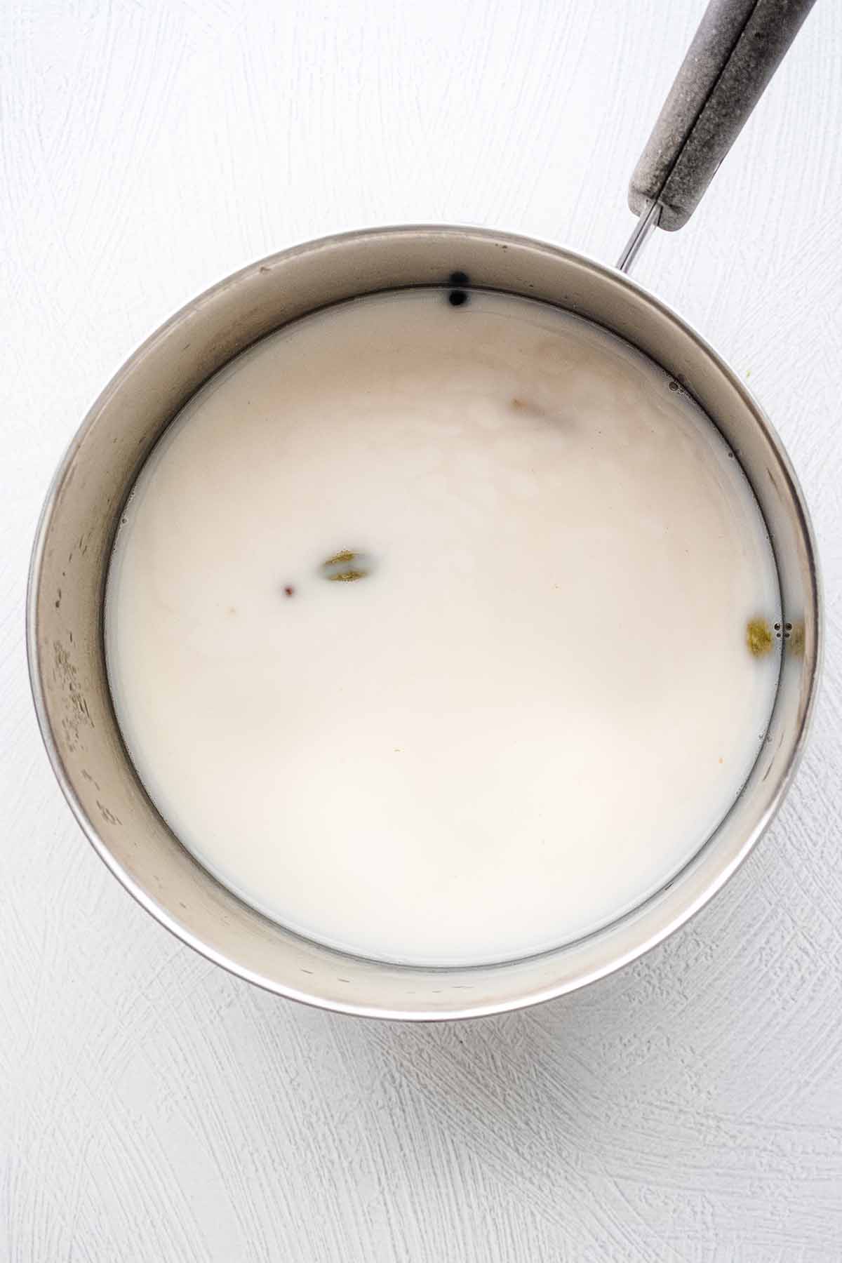 Overhead view of chai mixture in a saucepan with milk and sugar.