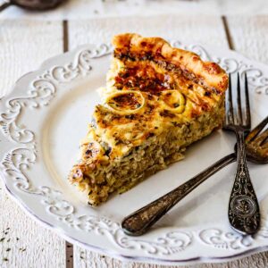 Slice of quiche on a white plate with two forks.
