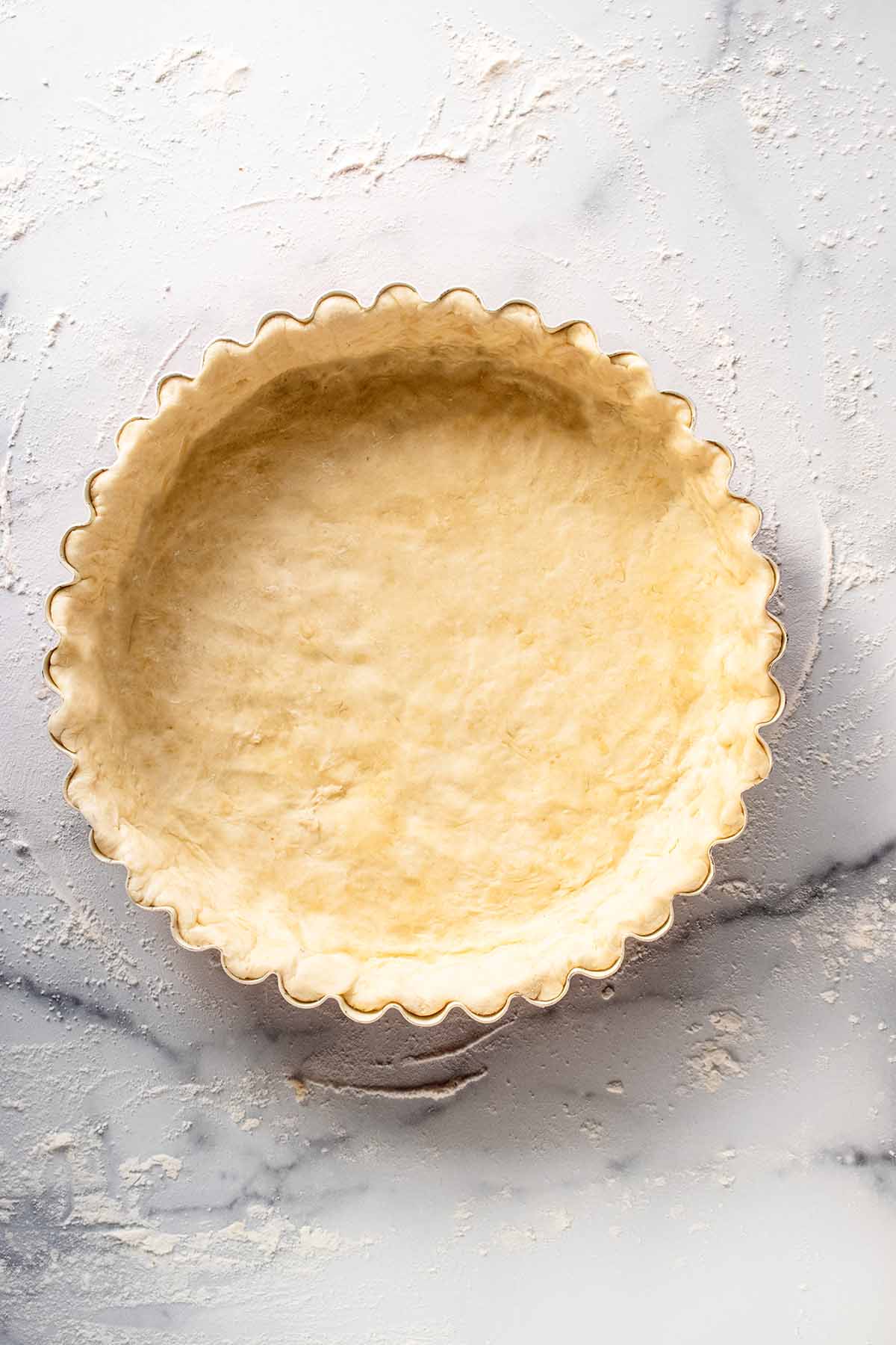 Raw crust dough in a tart pan with ends folded over inside the sides of the pan and pressed to fit.