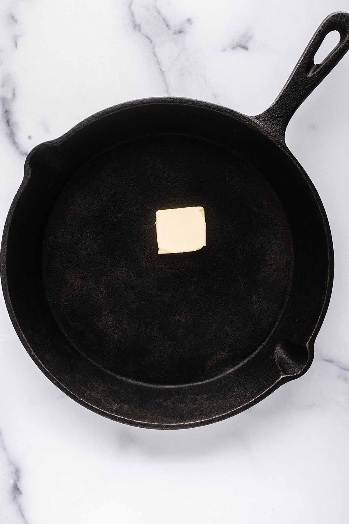 Overhead view of a pat of butter melting in a cast iron skillet.