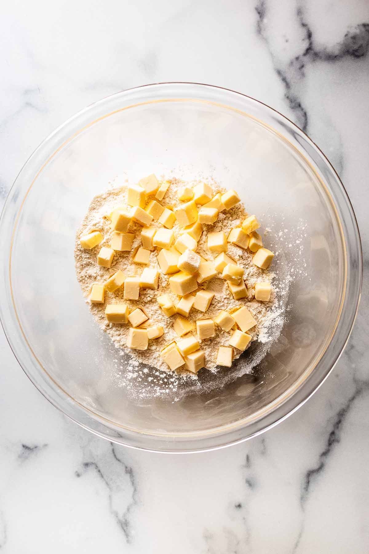 Overhead view of chopped butter in a large glass bowl with flour and salt.
