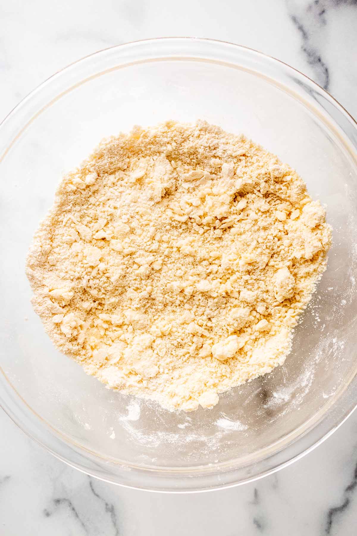 Overhead view of flour and butter mixture after being mixed in a large glass bowl.