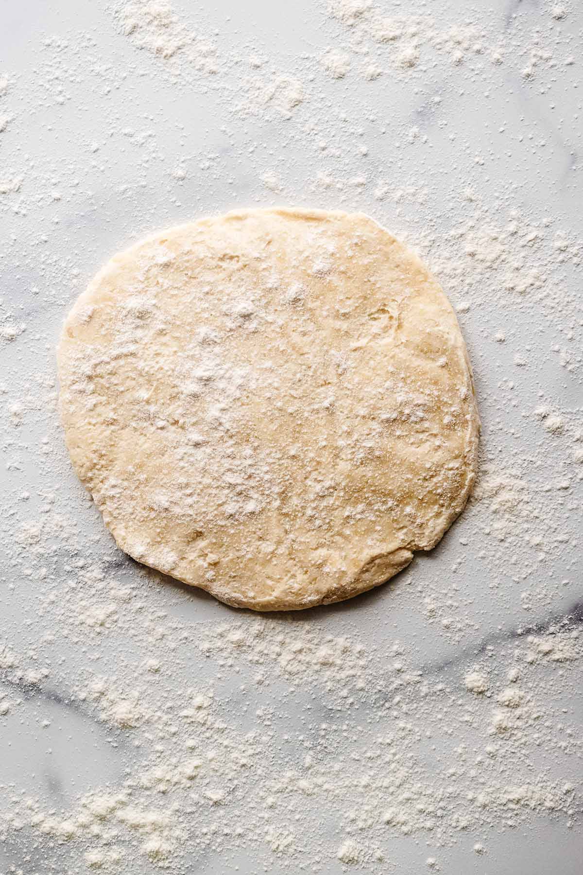 Raw crust dough on a floured marble countertop with flour sprinkled over the top
