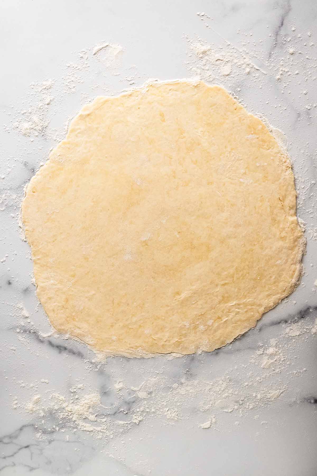 Raw crust dough rolled out to size on floured marble countertop