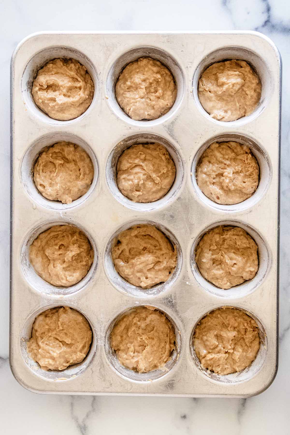 Overhead view of muffin batter in a 12-cup muffin tin.