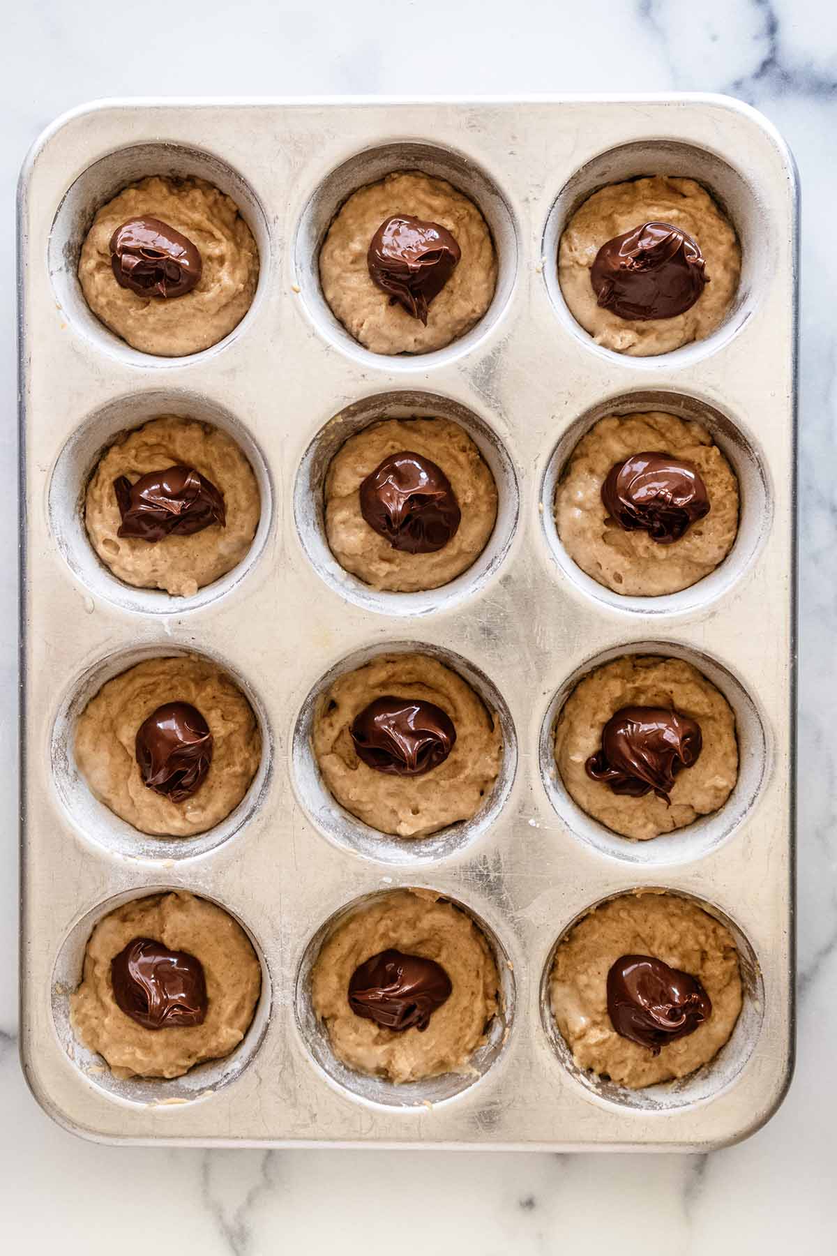 Dollops of Nutella on top of batter in a muffin tin.