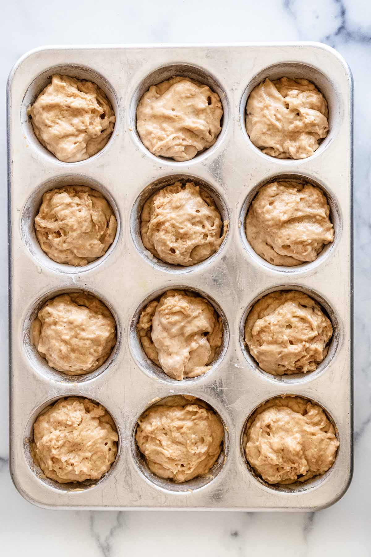 Muffin batter covering Nutella in a 12-cup muffin tin.