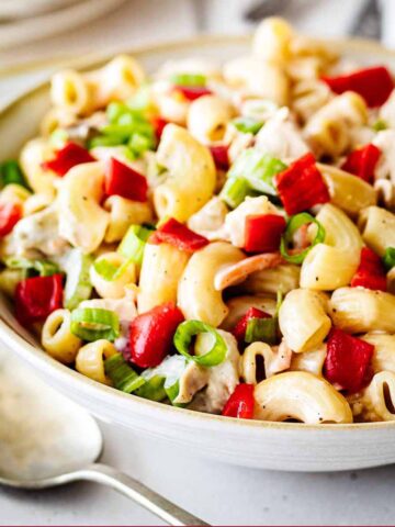 Closeup of chicken macaroni salad in a white bowl with a metal serving spoon.