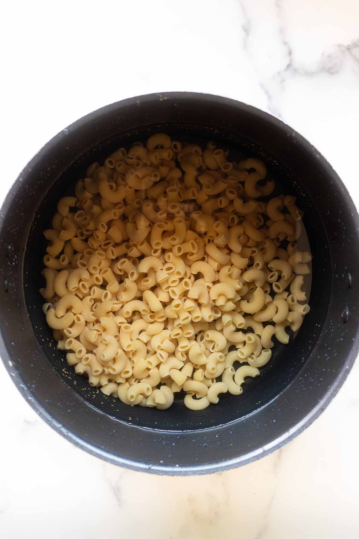 Overhead view of uncooked macaroni in a pot with water.