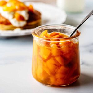 Mango compote in a small glass jar with a spoon