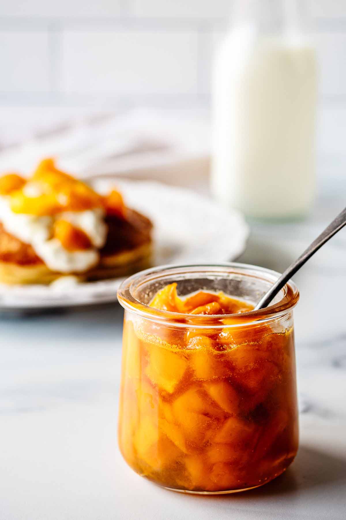 Mango compote in a small glass jar with a spoon