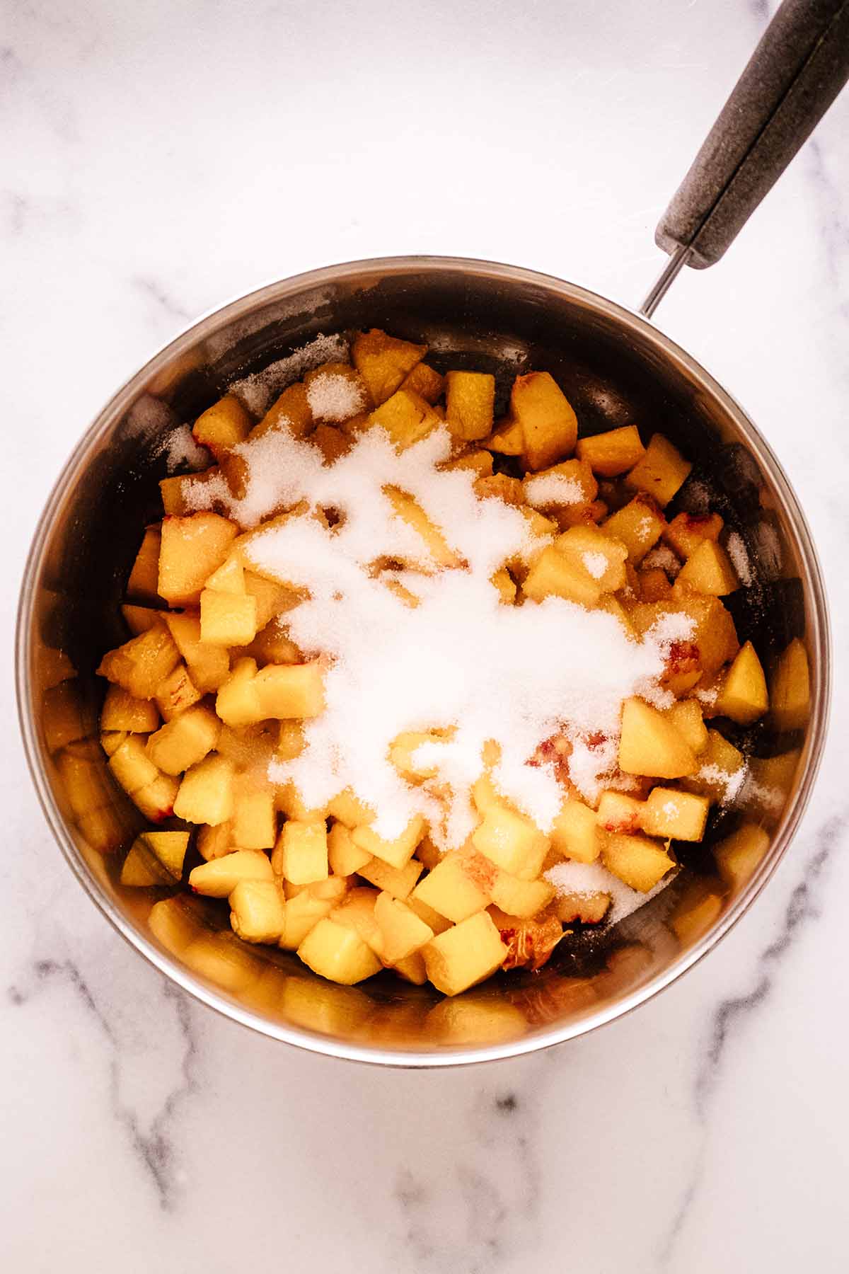 Overhead view of peach compote ingredients in a saucepan.