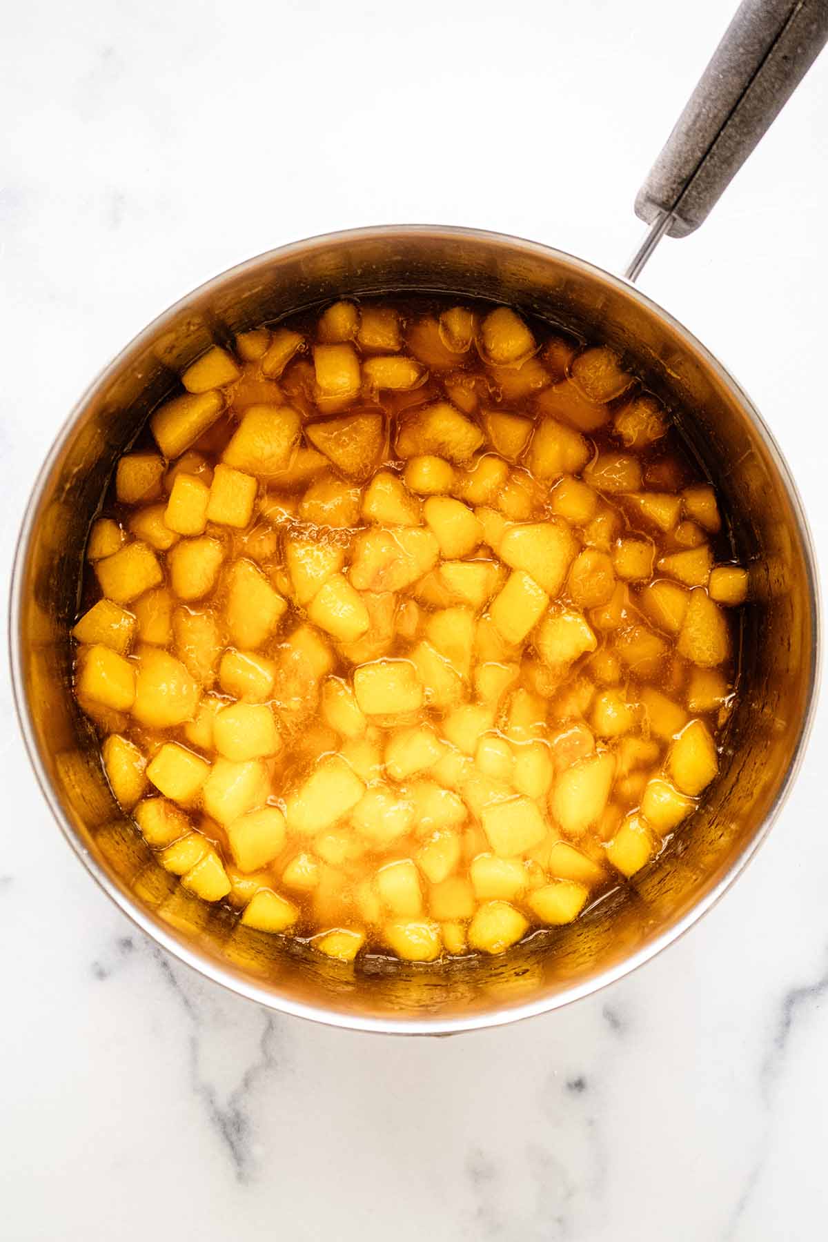 Overhead view of cooked peach compote in a saucepan.