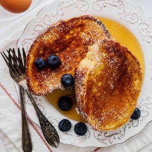 Overhead view of two slices of French toast on a white plate with two forks and whole blueberries.