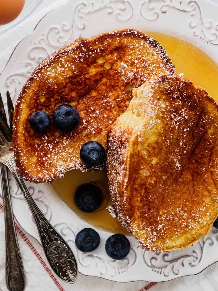 Overhead view of two slices of French toast on a white plate with two forks and whole blueberries.